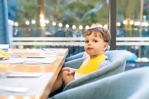 Young child sitting at dining table with bib, eating meal in bright modern .. Foto stock