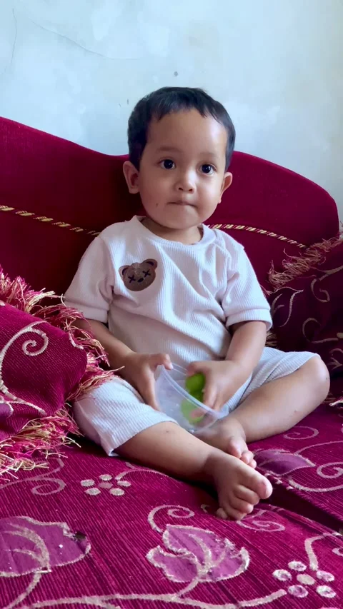 Young child sitting on a sofa playing with a green grape fruit Stock Footage 344104473