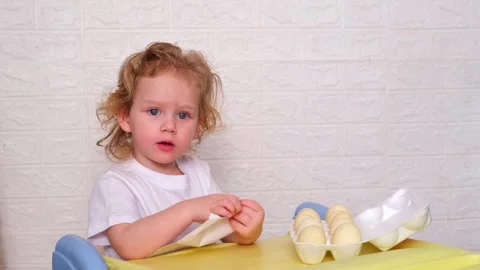 A young child is sitting at a table with a tray of eggs in front of him Stock Footage 330108921