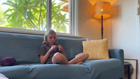 Young child skillfully knitting in a cozy chair with warm sunlight Stock Footage 308650048