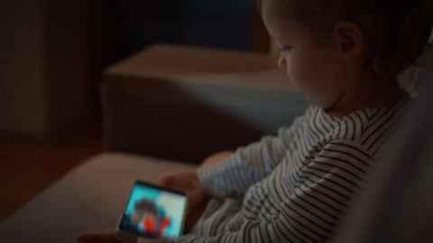 Young child snuggled up on the sofa is completely absorbed in vibrant cartoo Stock Footage 331301547