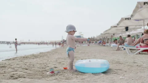 Young child with a sun hat plays with colorful toys near a blue inflatable ring Stock Footage 340900849