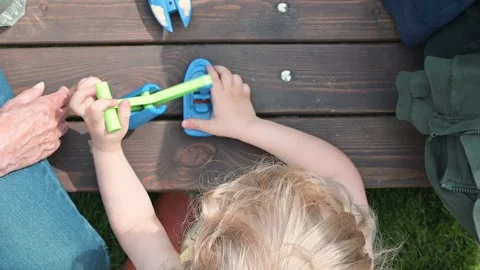 A young child uses tools to assemble a small model outdoors on a wooden surface. Stock Footage 338460205