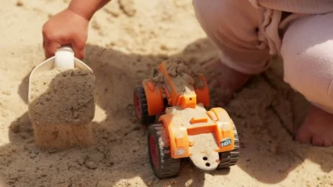 A young child is using a small scoop to dig in the sand while sitting next to an 動画素材 339030685