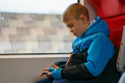Young Child Using Smartphone While Sitting by Train Window During Travel Stock Photos