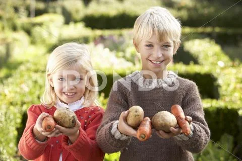 Young children in garden pose with vegetables Stock-Fotos