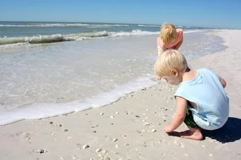 Young children picking up seashell on beach Stock Photos