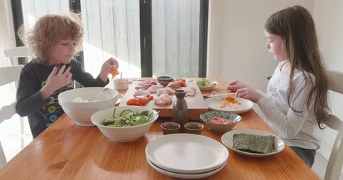 Young children sitting at a table eating a meal of sashimi off a wooden board Video stock 115545695