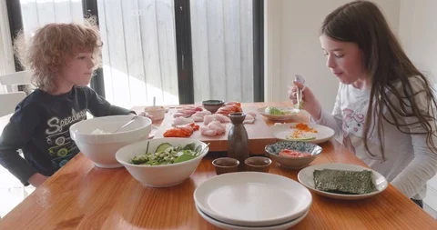 Young children sitting at a table eating a meal of sashimi off a wooden board Stock-Footage 115545761