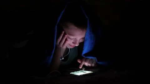 Young children using cell phone hidden under bed covers. 動画素材 134896808
