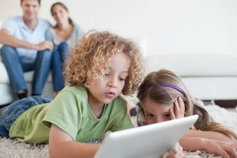 Young children using a tablet computer while their happy parents are watching 스톡 사진