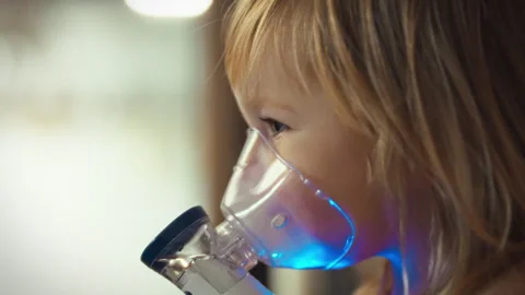 Young childs tiny hands carefully hold nebulizer device undergoing vital inh Stock Footage 331301590