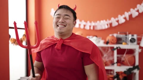 Young chinese man wearing devil costume holding trident at home 動画素材 236574841