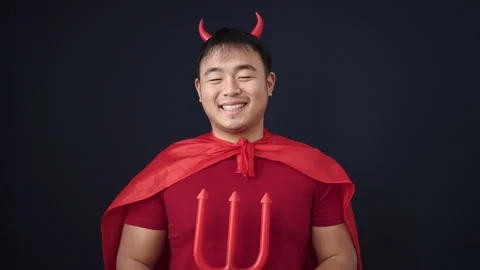 Young chinese man wearing devil costume holding trident over isolated black.. 動画素材 237309828