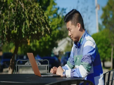 Young Chinese man working with laptop. On the summer terrace in the cafe Stock Footage 82018484