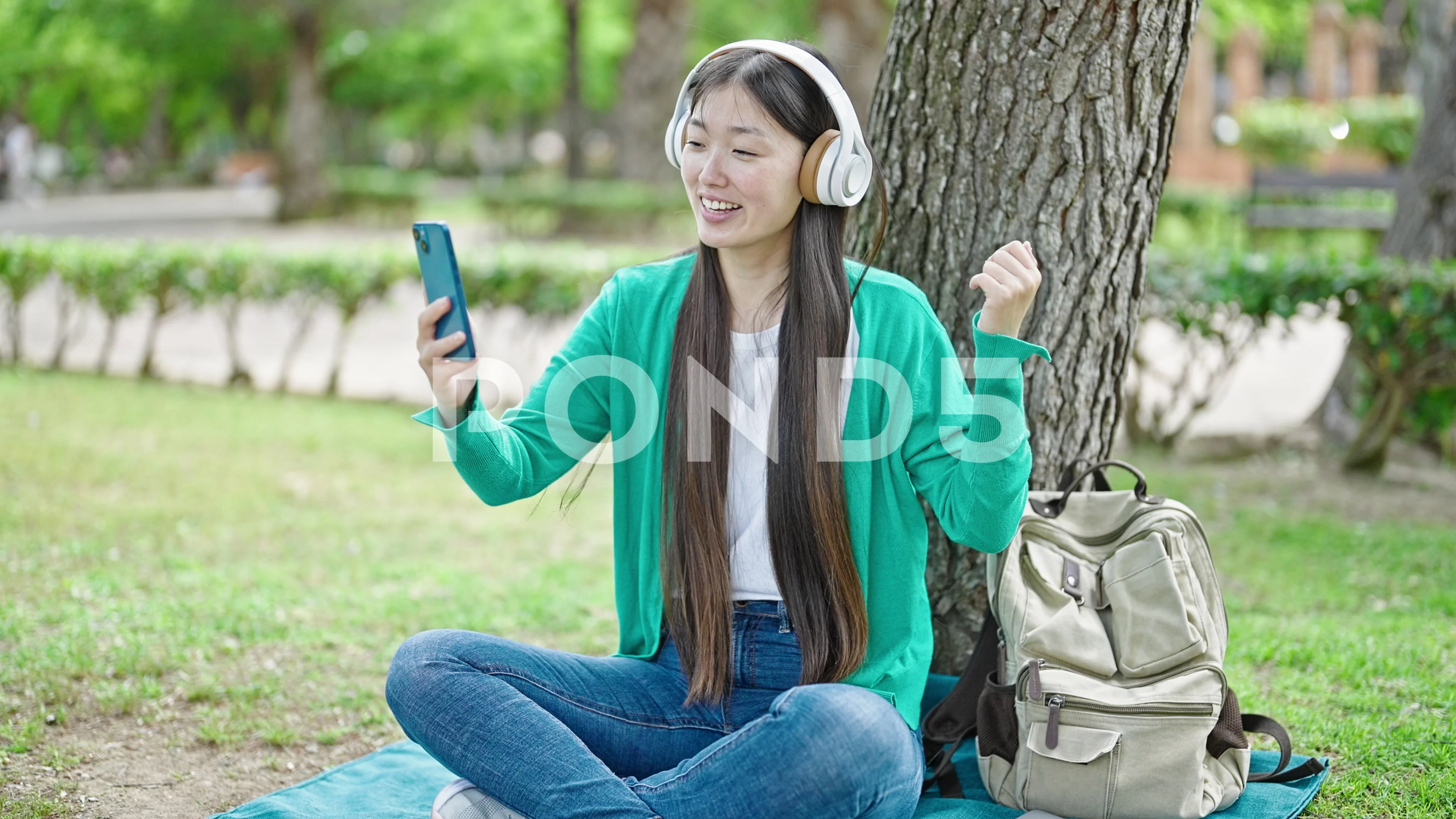 Young chinese woman having video call sitting on floor at park