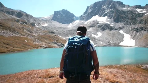 A young climber with a large hiking backpack goes to a mountain lake in summer Stock Footage 138444932