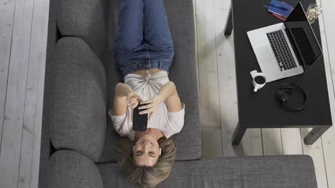 Young clothing lying down on sofa and having video call Video stock 233434885