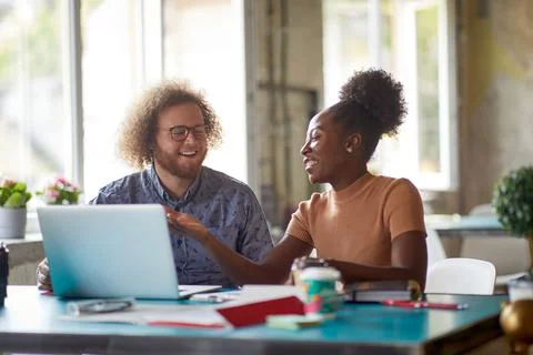 Young colleagues chatting while working at office together Stock Photos