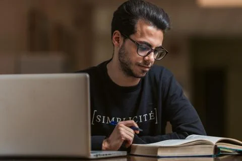 Young computer science student use a laptop and a book to study at the Stock Photos