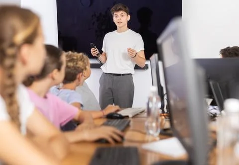Young computer science teacher standing near an interactive whiteboard tells new Stock Photos