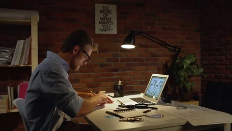 Young concentrated acrchitect with light beard and glasses sitting drawing with Stock Footage