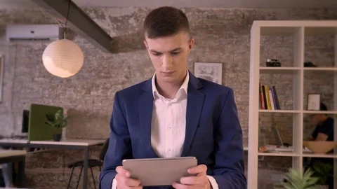 Young concentrated businessman is watching in tablet, watching at camera Video stock 91977369