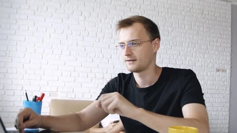 Young concentrated caucasian man is tapping on laptop, drinking from yellow c Stock Footage 111662328