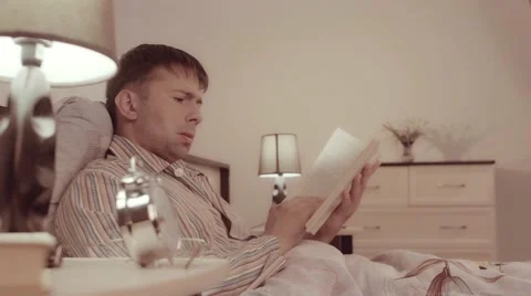 Young concentrated man reading a book in bed Stock-Footage 68420744