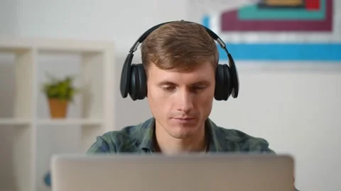 Young concentrated man using laptop and headphones at home Stock Footage 143555448
