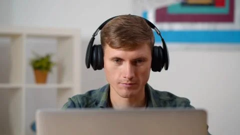 Young concentrated man using laptop and headphones at home 写真素材