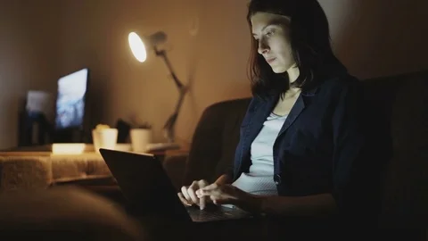 Young concentrated woman working at night using laptop computer and typing Stock Footage