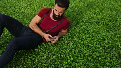 Young confident bearded man using his phone on the grass in a park Video stock 58663864