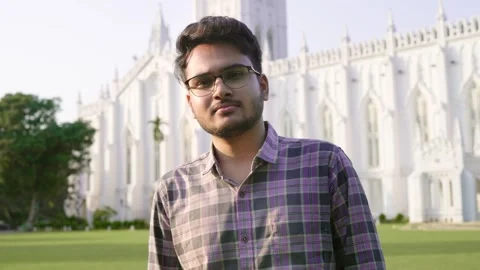 Young confident Indian man standing in front of white building looking at camera Stock Footage 267906751