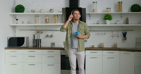 Young confident man is dancing and listening music in his kitchen Stock Footage 114641578