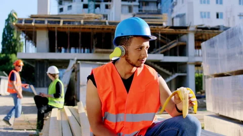 Young construction worker Afro American at the break time eating a banana and Stock Footage 146607468