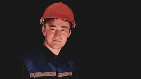 A young construction worker in an orange helmet looks at the camera and smiles Stock Footage 88063963