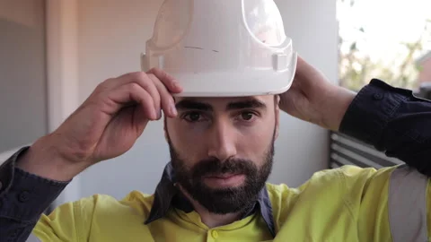 Young construction worker putting on hard hat in the morning looking serious Stock Footage 240392553