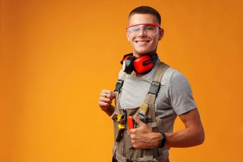 Young construction worker in uniform posing on yellow background in studio Stock Photos