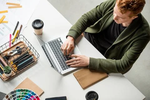 Young contemporary software developer pressing buttons of laptop keypad by desk 스톡 사진
