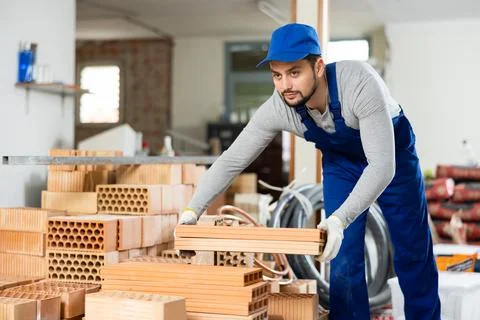 Young contractor stacking bricks on construction site indoors Stockfoto's