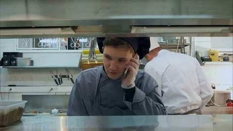 Young cook trainee talking on the phone in the professional kitchen Stock Footage 72325266