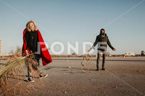 Young cool couple playing and battling with palm tree branches outdoors. Stock Photos