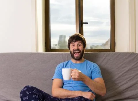 Young cool man sitting on a sofa at living room with a cup. Happy expression Stock Photos