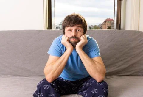 Young cool man sitting on a sofa in the living room with bored expression, ar Stock Photos
