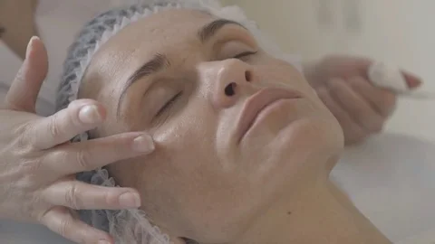 Young cosmetologist puting cream on the face of the client in the beauty salon Stock Footage