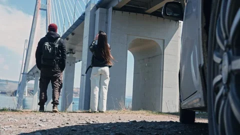 A young couple arrives under the cable-stayed bridge and takes photos.  Stock Footage 308920230