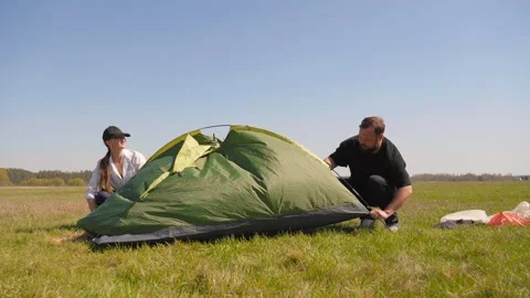 Young couple assembling a camping tent together in a sunny field Видео 344602068