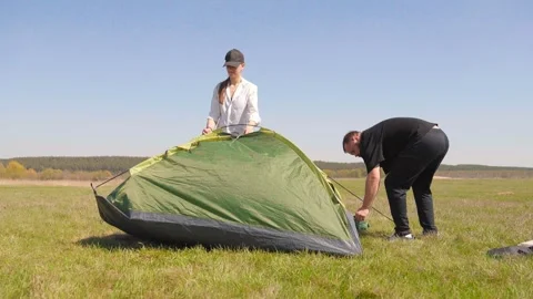 Young couple assembling a camping tent together in a sunny field 스톡 동영상 344602221