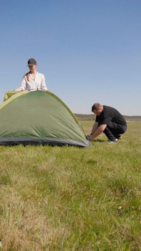 Young couple assembling a camping tent together in a sunny field 库存影片 344602268